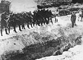Members of an Einsatzkommando firing at men standing at the bottom of a trench